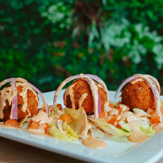 Three breaded croquettes at Maria Mia Tex-Mex Cantina, topped with veggies and red onion slices.