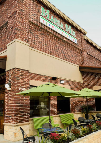 Red brick exterior with green umbrellas at Maria Mia Tex-Mex Cantina Restaurant Bar in College Station, Texas.