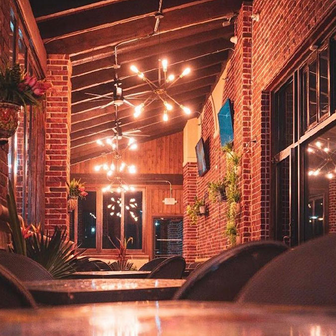 Warmly lit brick patio at Maria Mia Tex-Mex Cantina in Texas, with modern chandeliers and plants.