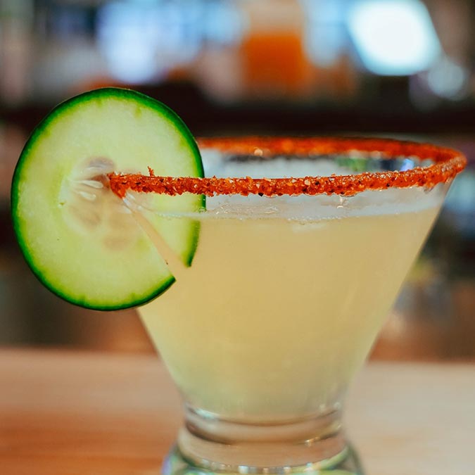 A Texas-inspired cocktail with a chili rim and cucumber slice garnish in a martini glass.