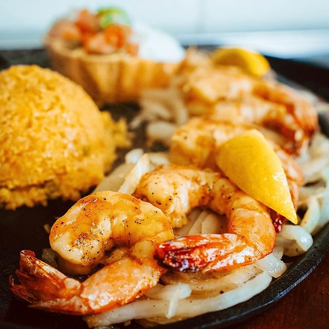 Grilled shrimp with onions, yellow rice, and lemon at Maria Mia Tex-Mex Cantina in Texas.