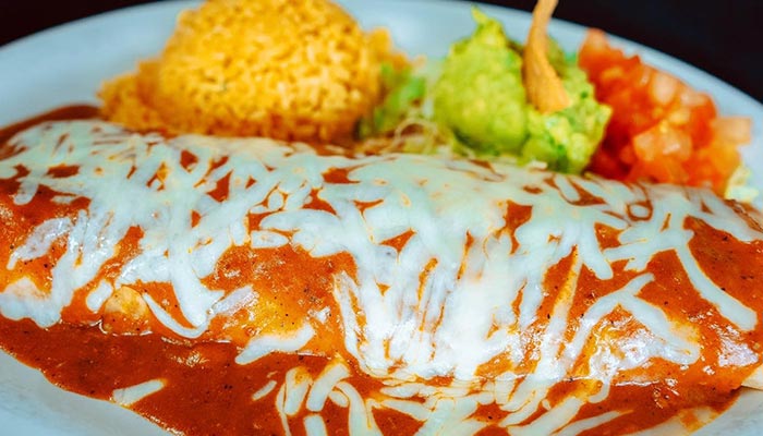 A Texas-style smothered burrito with cheese, rice, guacamole, and pico de gallo on the side.
